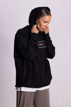 Person, die einen schwarzen Falkenstern-Hoodie mit Falkenmotiv auf dem Rücken vor einem einfarbigen Hintergrund trägt