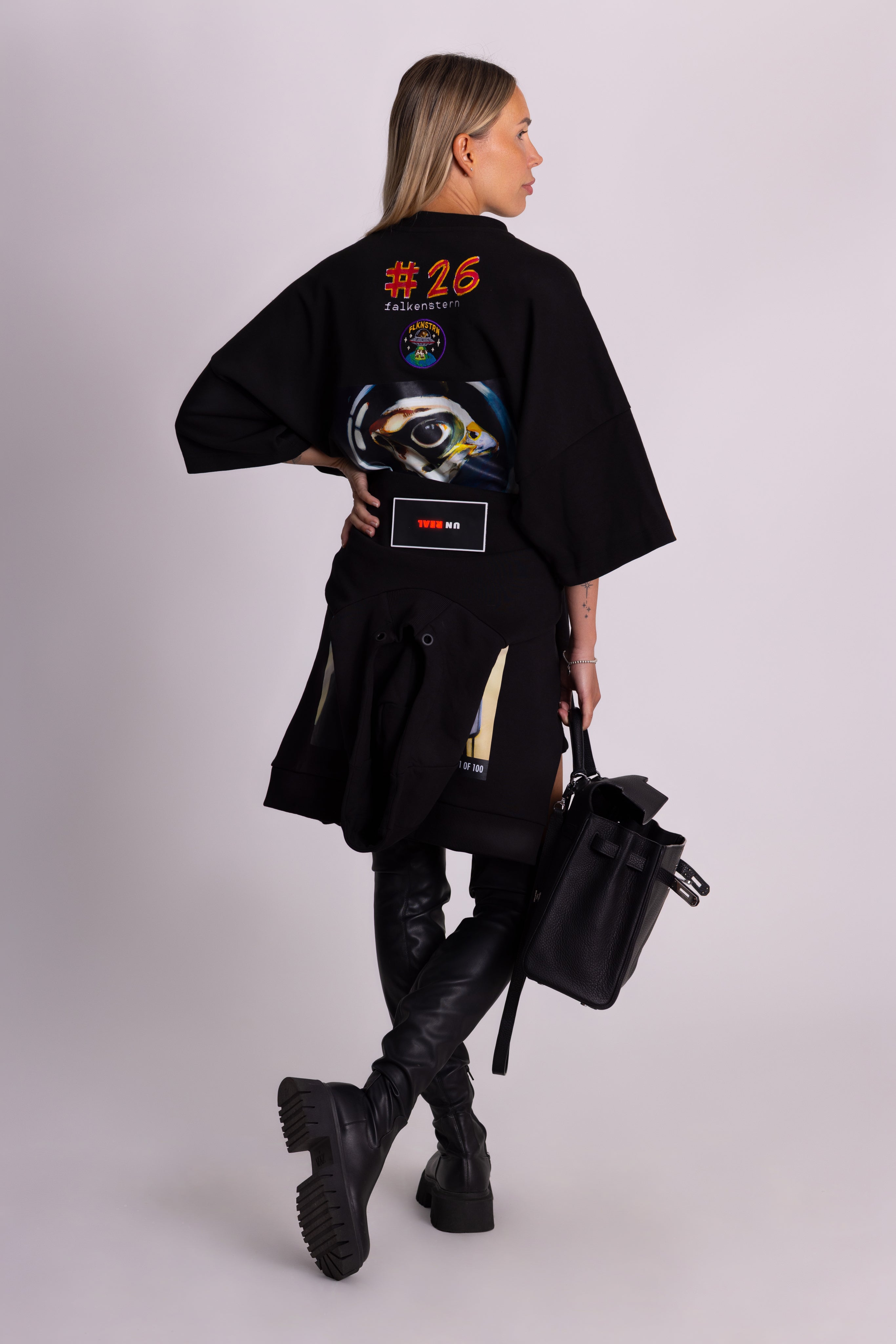 Person, die ein schwarzes Falkenstern-T-Shirt mit Falkenmotiv auf dem Rücken vor einem einfarbigen Hintergrund trägt