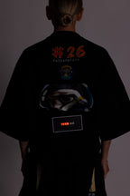 Person in einem schwarzen T-Shirt mit Grafikdesign und Text auf dem Rücken vor dunklem Hintergrund