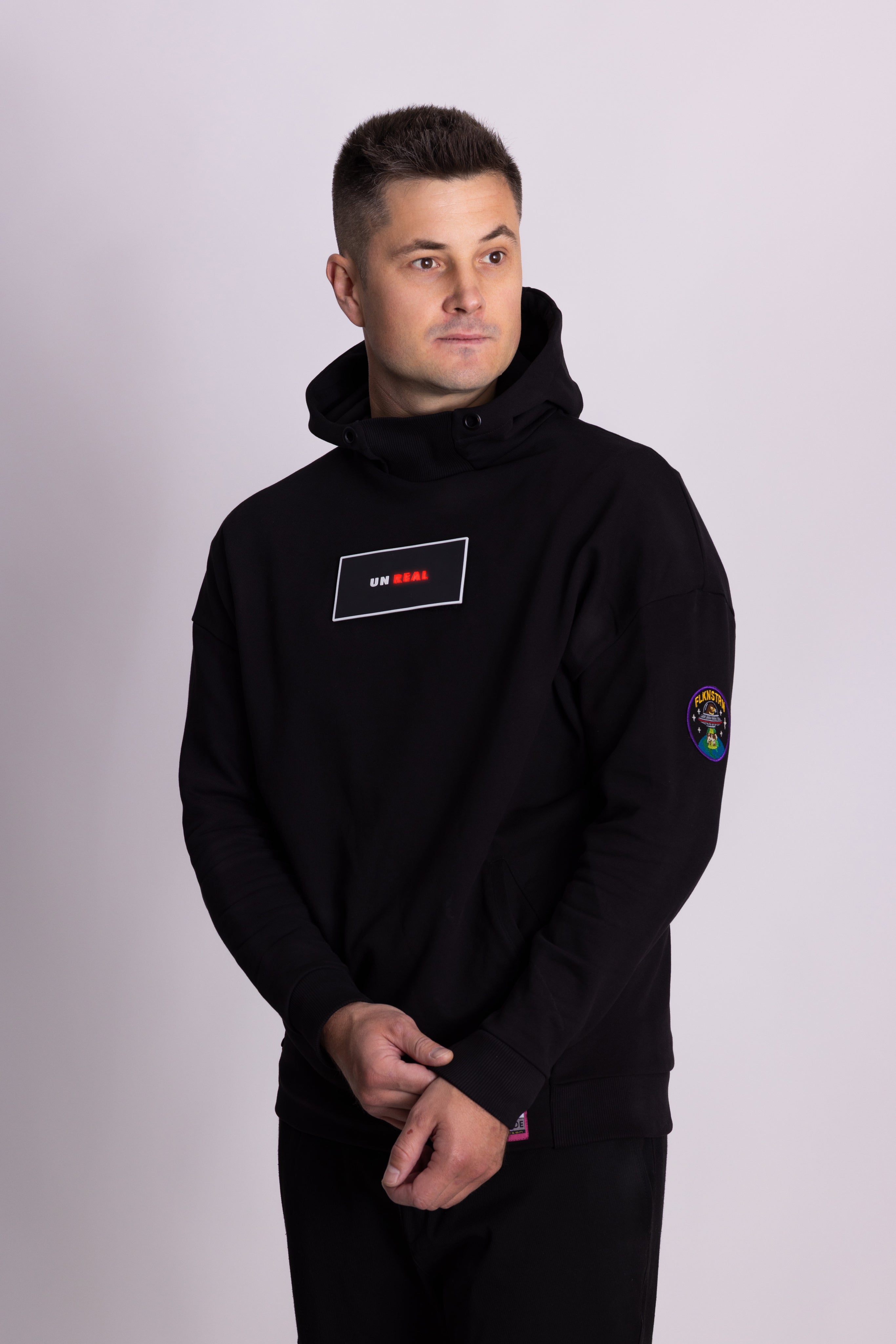 Mann mit schwarzem Kapuzenpullover mit Logos auf hellgrauem Hintergrund